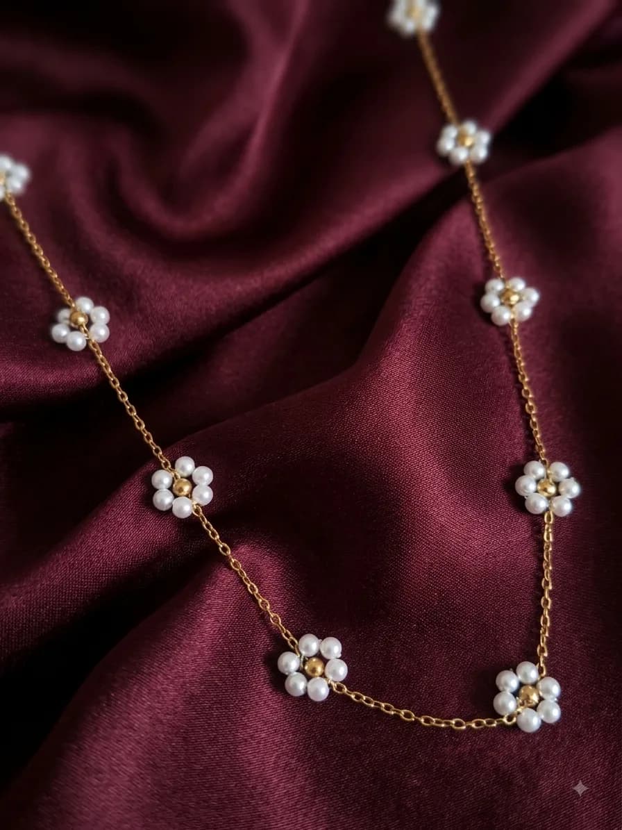 A gold-plated chain set with white pearl daisies with gold centres, on oxblood satin